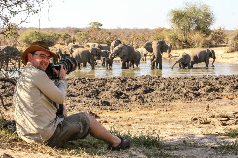 photographer sitting watching elephants at waterhole, Hwange NP